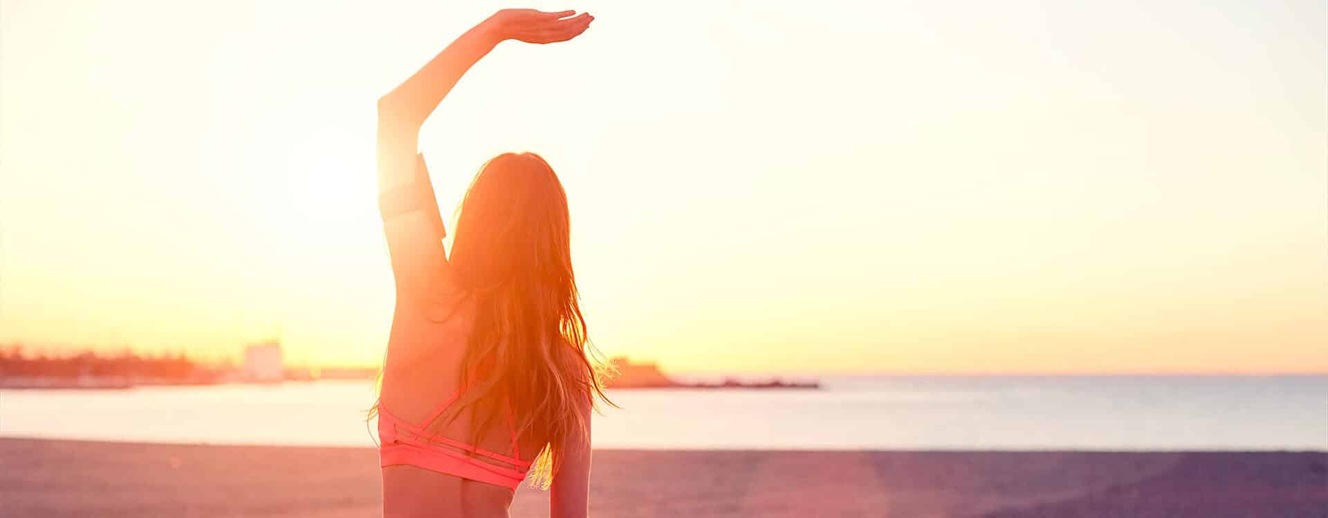 Junge Frau macht Yoga am Strand bei Sonnenuntergang und streckt ihre Wirbelsäule dabei durch