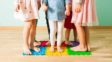 Beispielbild für die Köhlerkrankheit - sechs Kinder stehen auf einem Puzzleteppich am Boden