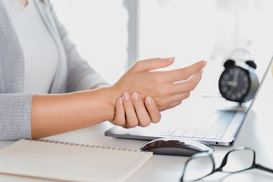 Frau hält sich das Handgelenk vor Schmerzen nach langer Arbeit am Laptop